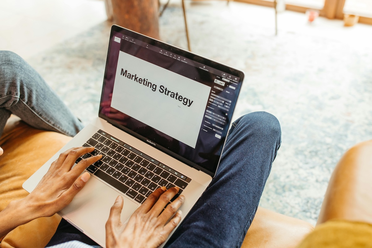 A person using a laptop on their lap showing the words ‘marketing strategy’